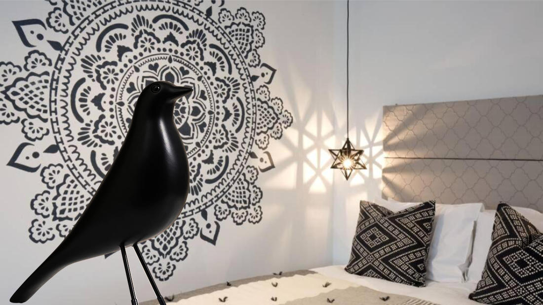 Montage of blackbird figurine on a bed with large grey and white cicular wall motif behind it